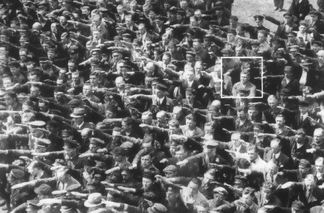 No destaque vemos August Landmesser sem realizar a saudação nazista, em uma solenidade onde o próprio Hitler estava presente